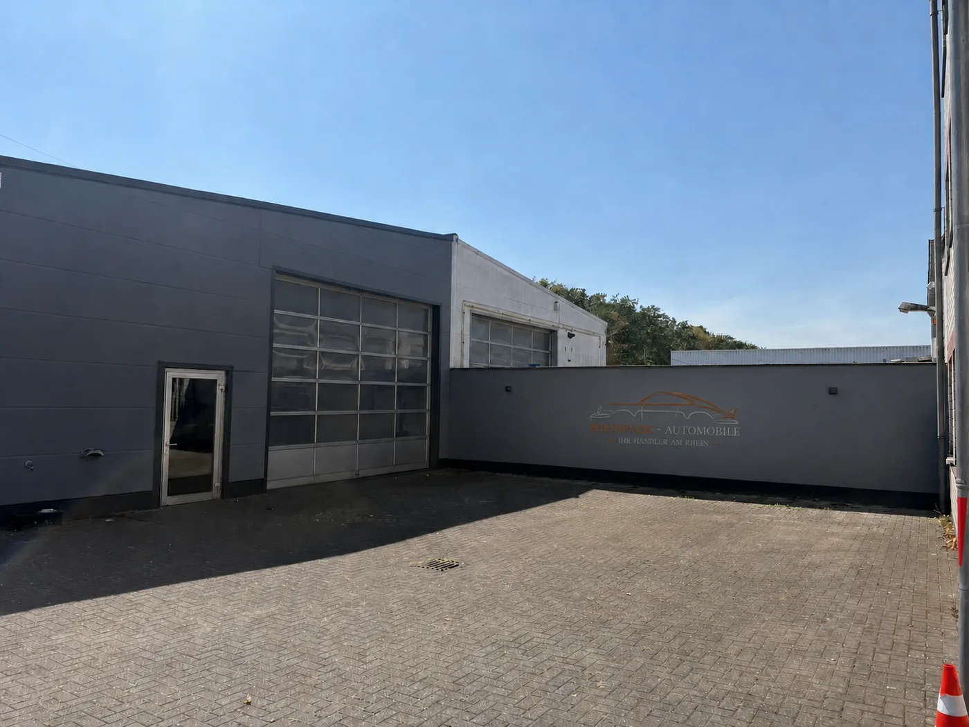 Bearbeitete Außenansicht von RheinPark Automobile mit visualisiertem Wandlogo und freiem Hof