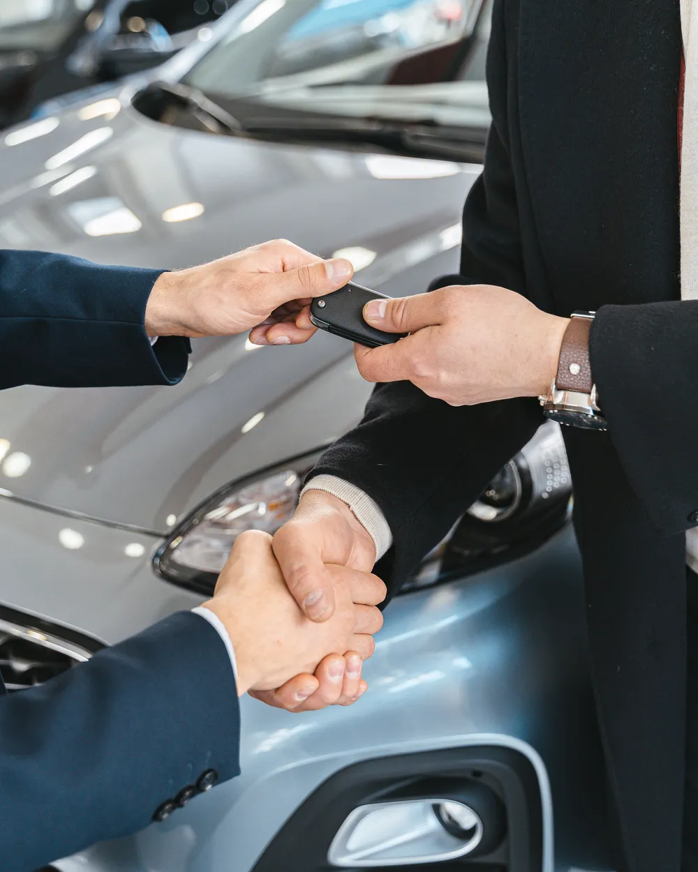 Fahrzeugschlüssel und Abnahmeprotokoll auf einem Klemmbrett vor geöffneter Motorhaube